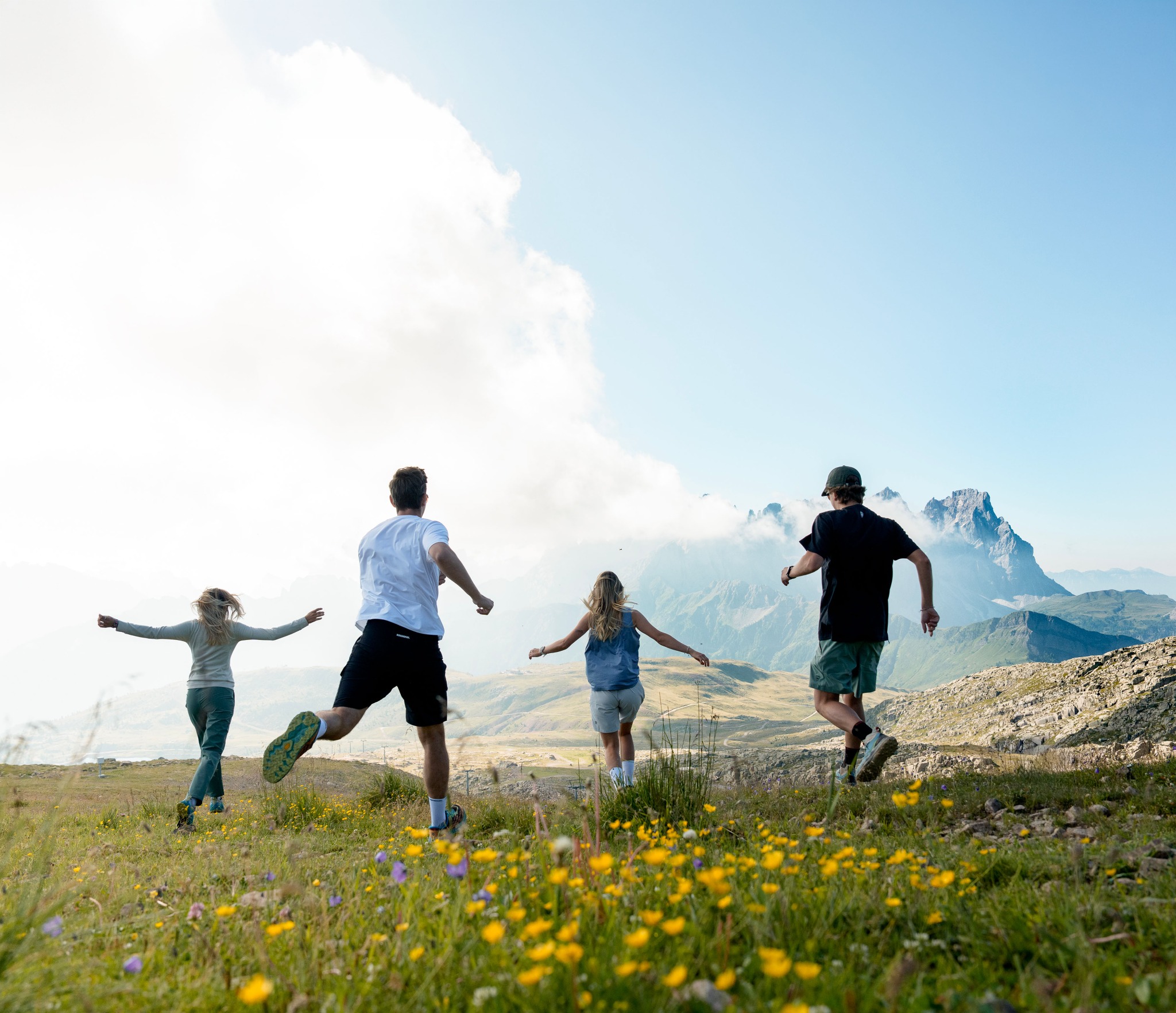 Famiglia che corre sui prati fioriti del Col Margherita, con le Dolomiti sullo sfondo