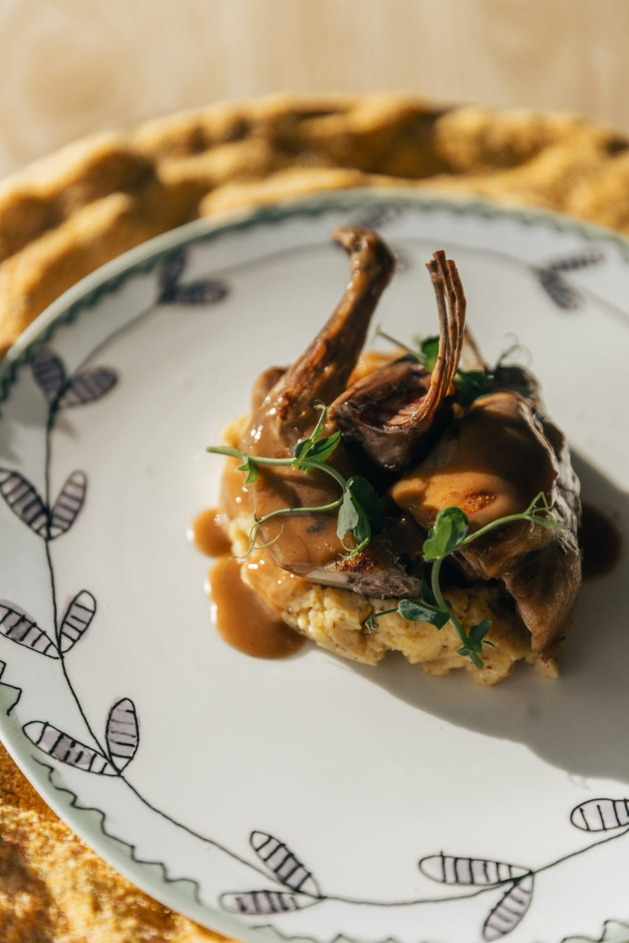 Piatto di carne con salsa e polenta, decorato con germogli di pisello