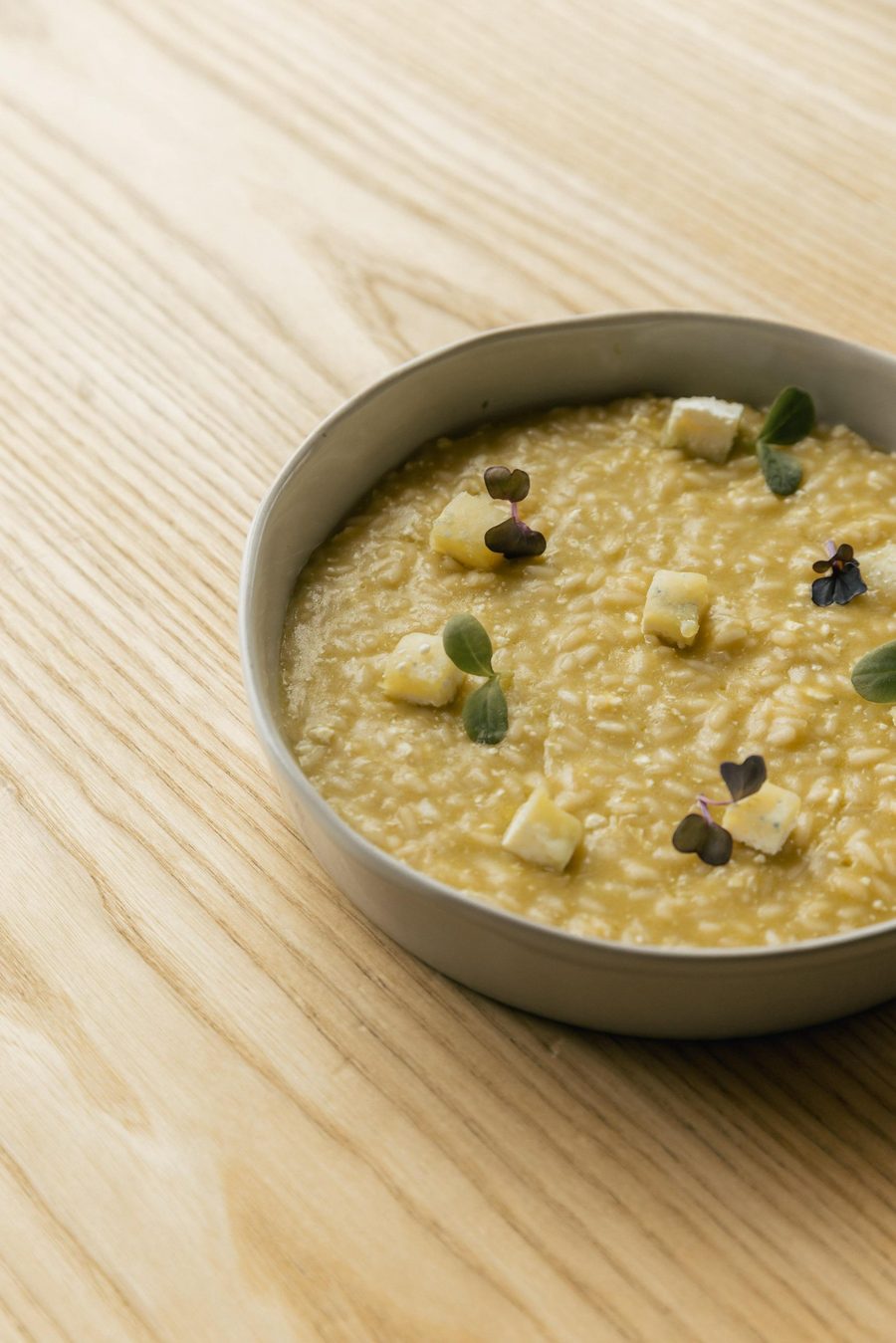 Risotto servito in una ciotola di ceramica, con cubetti di formaggio e germogli